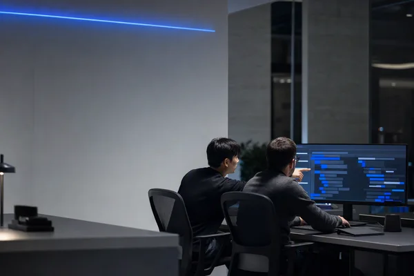 Two developers reviewing code together on a large monitor in a quiet office at night