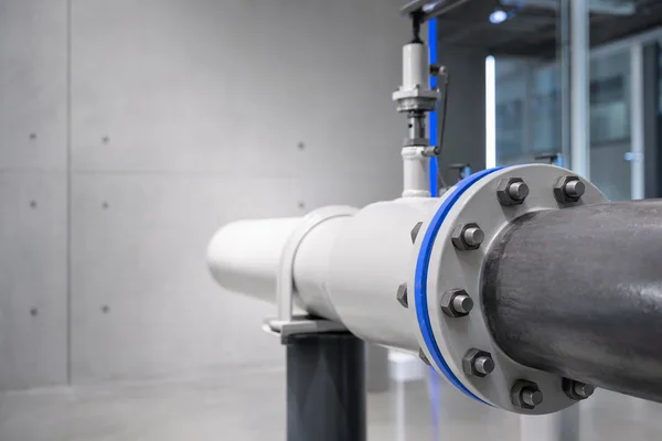 Two industrial pipes joined by a bolted flange in a clean plant room