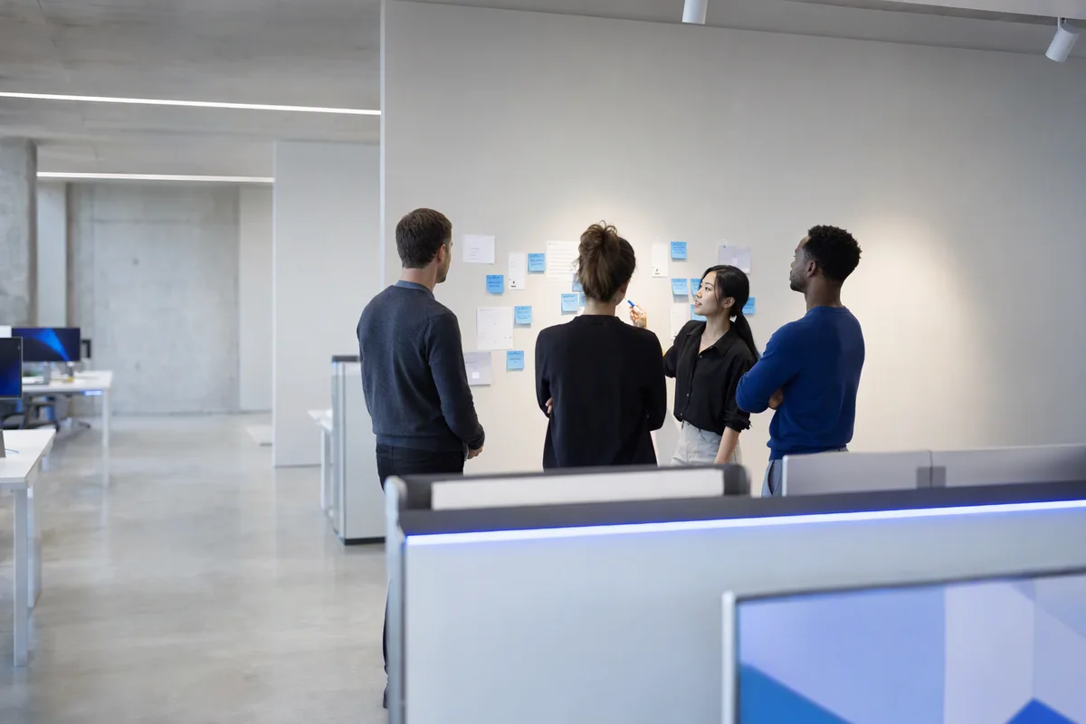 A small team at a whiteboard wall with sticky notes, one person explaining while others listen